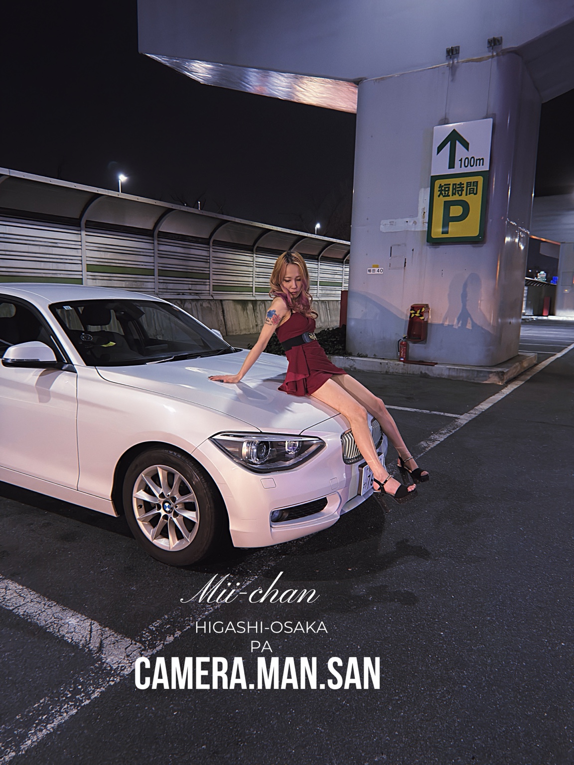 Portrait in a red dress beside a white BMW at night
