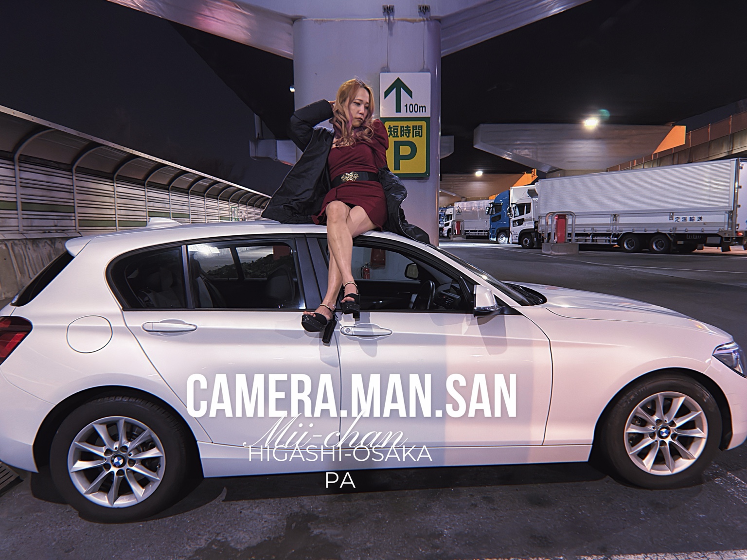 Portrait seated beside a white BMW in a parking area at night