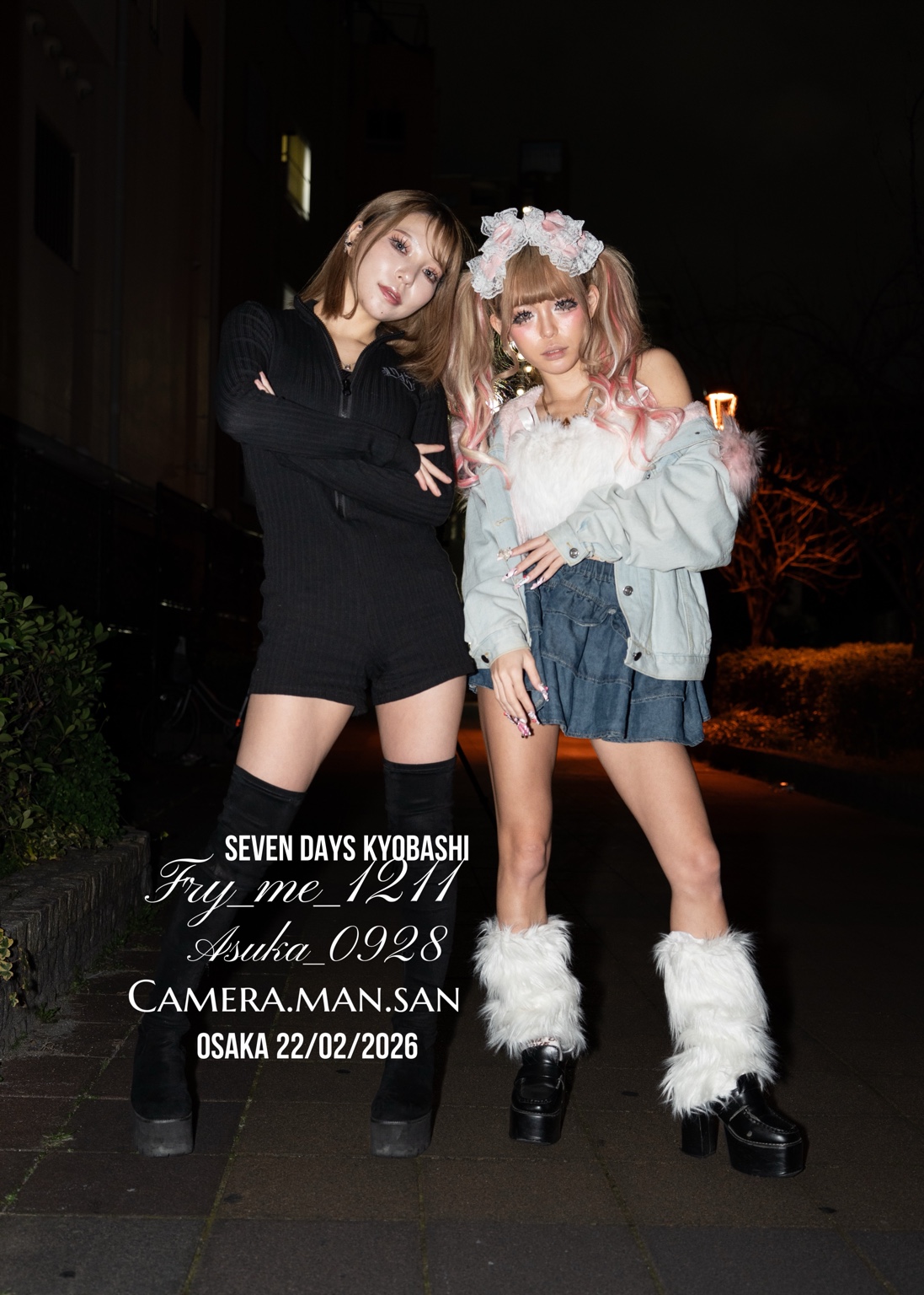 Two people posing side by side on a nighttime street